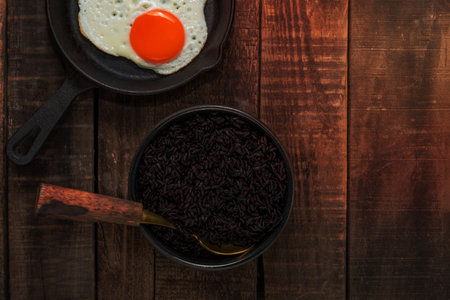 Black rice in bowl dish have fried egg in pan isolated on wood background close up, top view, healthy food and drink concept.の写真素材