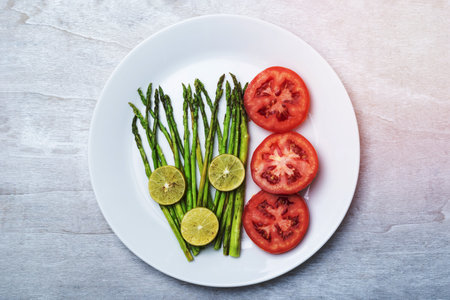 Asparagus grill with lemon and tomato in plate on white wood background top view, close up, healthy food concept.の写真素材