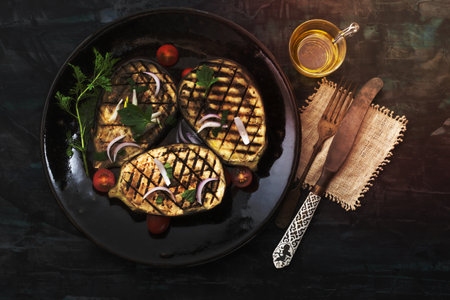 Grilled eggplants in plate has fork on isolated on black wood background close up, top view, healthy food concept.の写真素材
