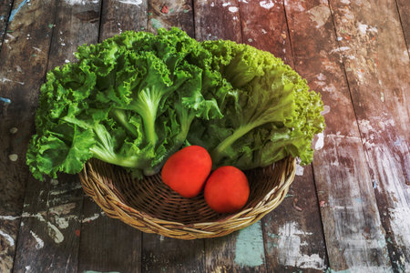 Lettuce and tomato in basket on wood background close up, top view, healthy food concept.の写真素材