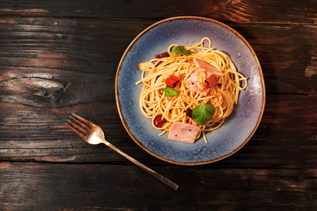 Pasta spaghetti garlic ham dried chili in blue plate isolated on wood background close up, top view, food concept.の写真素材