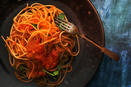 Pasta spaghetti with tomato sauce in black plate on blue wood background, top view, Italian food concept.の写真素材