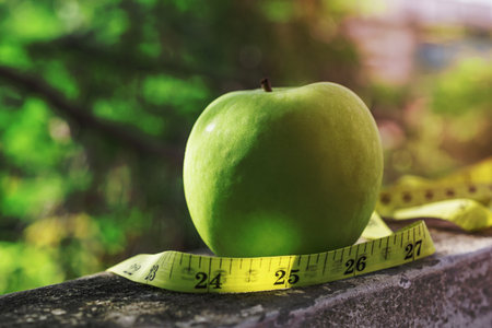 Measure tape and green apple on stone background close up, healthy food concept.