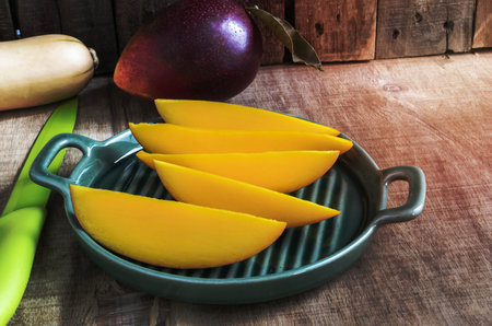 Red Mango fruit sliced in plate isolated on rustic wood background, top view, healthy food concept.の写真素材