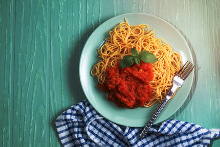 Pasta spaghetti with tomato sauce in green plate on green background, top view, Italian food concept.の写真素材