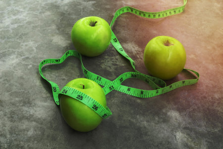 Measure tape and green apple on stone background close up, healthy food concept.の写真素材