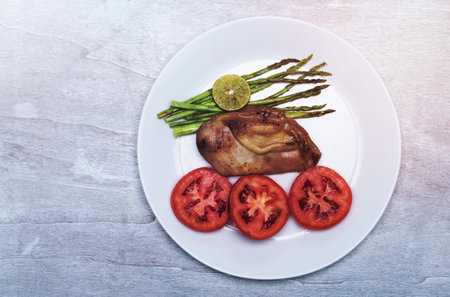 Chicken grill with lemon and asparagus tomato in plate on white wood background top view, close up, healthy food concept.の写真素材