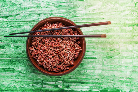 Rice red in bowl isolated on green background has chopsticks close up, top view, Asian food and drink concept.の写真素材
