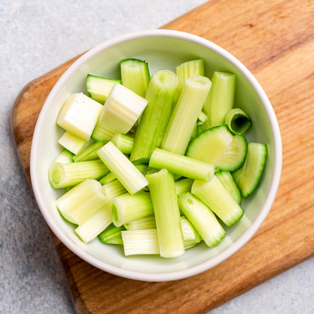Fresh Chopped Celery Slices in White Bowl with Celery Sticks on Bamboo Cutting Boardの素材