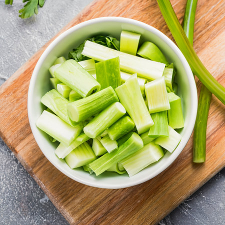 Fresh Chopped Celery Slices in White Bowl with Celery Sticks on Bamboo Cutting Boardの素材