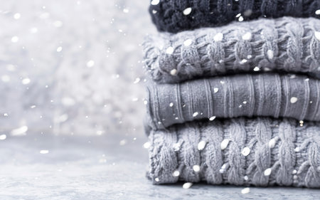 a stack of knitted winter sweaters in several shades of gray on gray background. falling snowの素材