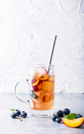 Cup and jar of peach ice tea served with fresh peach an berries over white textire backgroundの素材