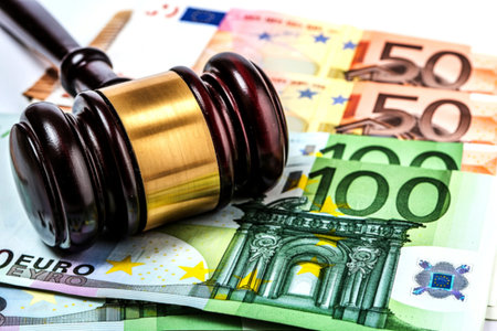 A dark wooden gavel with a brass band lies on a spread of euro banknotes, including 100 and 50 euro bills, signifying legal and financial proceedings.の素材
