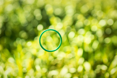A vibrant green ring is suspended in the air, set against a softly blurred backdrop of lush green...