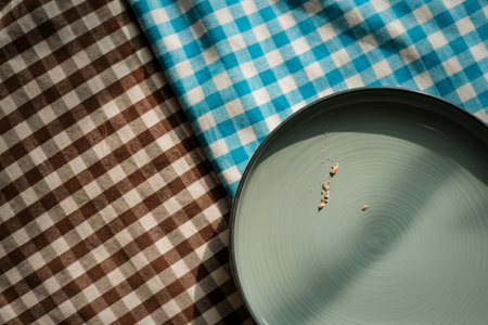 A light blue and white checkered picnic blanket is partially covered by a brown and white checkered...
