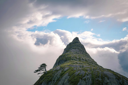 A solitary, jagged mountain summit rises dramatically towards a turbulent sky filled with swirling clouds and hints of blue.の写真素材