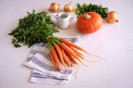 A collection of vibrant, fresh vegetables including carrots, pumpkin, and onions, arranged on a white surface with a striped napkin.の写真素材