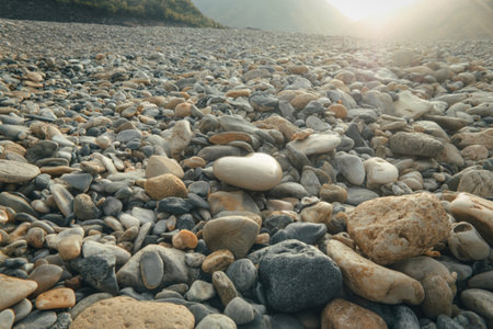 A textured ground of various sized river stones, with a bright, hazy sun illuminating the scene from the distance.の写真素材