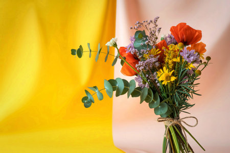 A colorful bouquet of wildflowers, including poppies and daisies, is tied with twine and set against a backdrop of draped yellow and pink fabric.の写真素材
