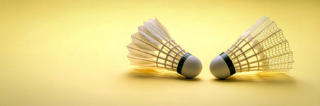 Two white badminton shuttlecocks with feathered skirts are positioned upright, facing each other on a soft yellow surface.の写真素材
