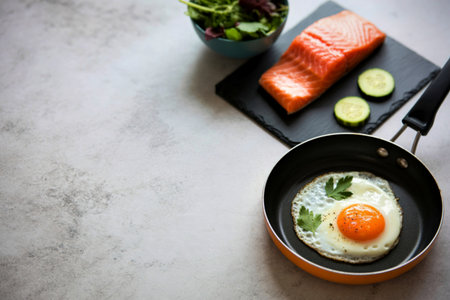 A delicious and nutritious breakfast featuring a fillet of salmon, a perfectly fried egg, cucumber slices, and a side of fresh salad.の写真素材