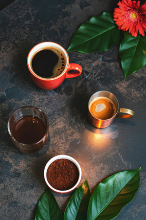 A top-down view showcases various coffee preparations, including espresso and grounds, alongside a vibrant red flower and lush green leaves.の写真素材