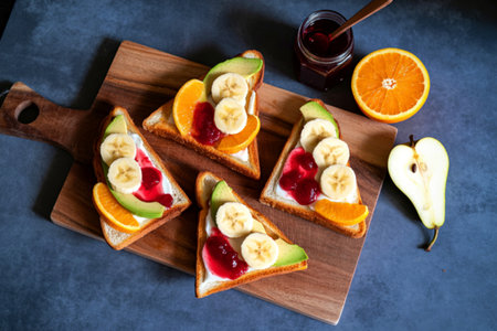 Four triangular toast slices topped with yogurt, banana, berries, and orange slices, served on a wooden board.の写真素材
