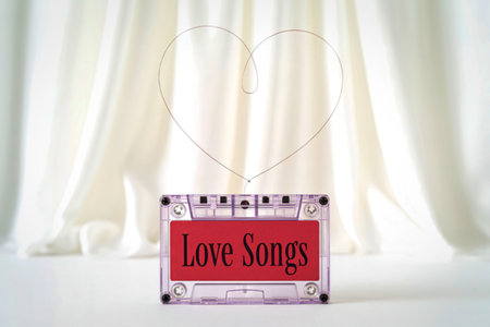 A clear cassette tape labeled 'Love Songs' in red sits centered against a backdrop of soft, white draped fabric, evoking nostalgia and romance.の写真素材