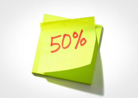 A bright yellow sticky note with the number fifty and a percent sign written in red ink, casting a subtle shadow.の写真素材
