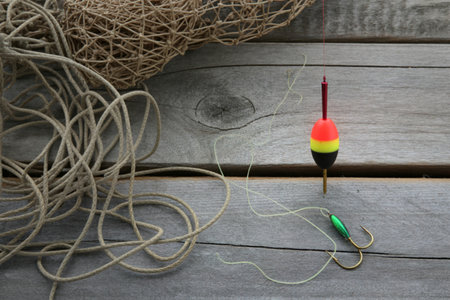 A fishing float with red yellow and green bands sits next to a fishing hook on a weathered wooden surface with a fishing net.の写真素材