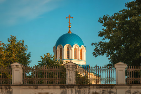A majestic church with a vibrant blue dome and arched windows stands behind a decorative metal fence, surrounded by lush green trees.の写真素材