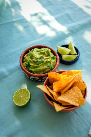 A vibrant bowl of homemade guacamole is served with crispy tortilla chips and fresh lime wedges, perfect for dipping and enjoying.の写真素材