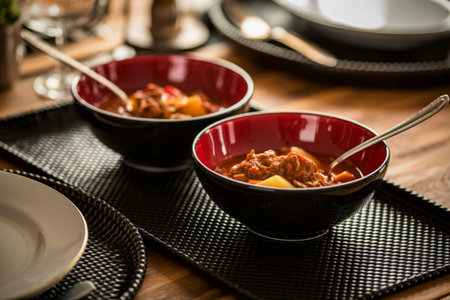 Two dark bowls with red interiors hold a rich, chunky stew. Spoons are resting in each bowl, ready for a meal.の写真素材