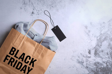 A brown paper shopping bag with "Black Friday" printed on it, containing striped clothing and a black tag, lies on a textured surface.の写真素材