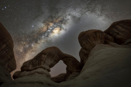The Milky Way galaxy stretches across a dark night sky above unique desert rock formations and arches.の写真素材
