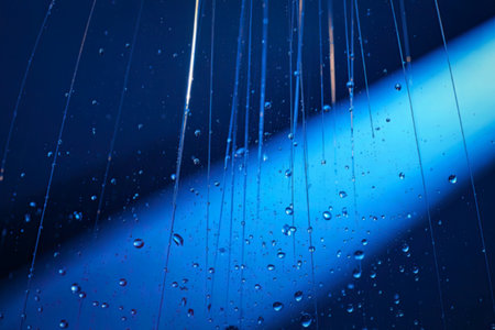 A close-up image of blue raindrops falling against a dark blue background, creating a serene and...