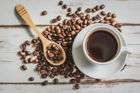 A white cup of coffee is placed on a wooden surface, surrounded by scattered coffee beans and a wooden spoon.の写真素材