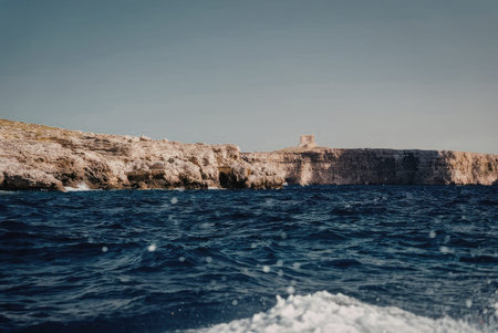 a body of water with a rocky cliff in the background, possibly an ocean or sea with a clear blue sky