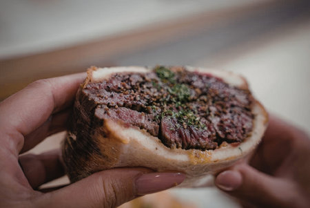 A close-up shot of a person holding a burger with a large beef patty, garnished with green herbs, on...