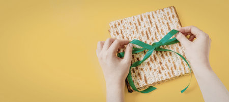 A person's hands are shown tying a green ribbon around a gift wrapped in brown paper on a yellow...