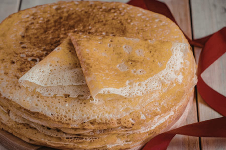 A stack of pancakes with a slice cut out, placed on a wooden surface with a red ribbon