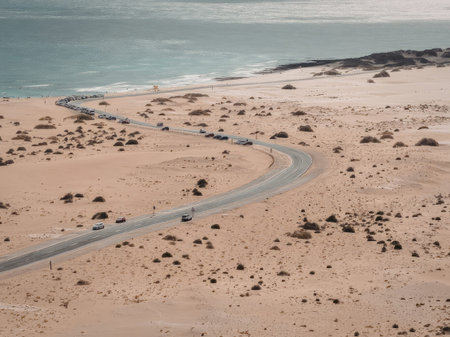 An aerial view of a winding road that runs along a desert coastline, with the ocean on one side and...