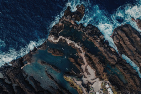 An aerial view of a rugged rocky coastline with waves crashing against the shore, showcasing the...
