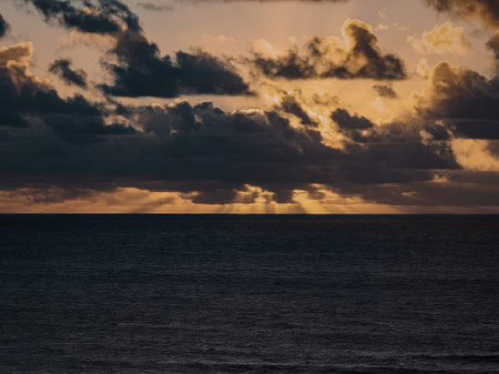 A serene ocean landscape at sunset with vibrant orange clouds reflecting on the water's surface,...