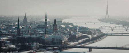 Aerial view of a city with snow-covered buildings, a river, and bridges in a foggy atmosphere.