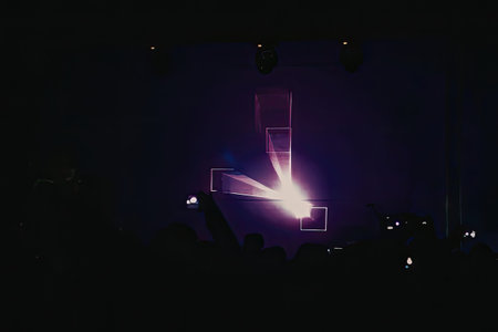 A darkened concert stage with a bright purple light shining on it, with a crowd of people in the...