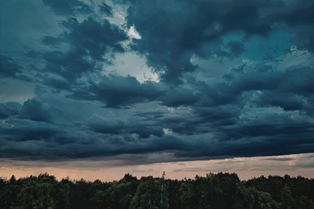 A serene landscape of dark clouds over a forest at sunset, with the sky transitioning from blue to...