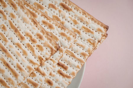 A close-up image of a toasted matzo on a pink background, showcasing its crispy texture and golden...