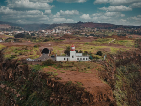An aerial view of a white lighthouse with a red roof situated on a cliffside, overlooking a town and...
