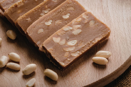 A close-up of a brown dessert with nuts on a wooden board, cut into rectangular slices.